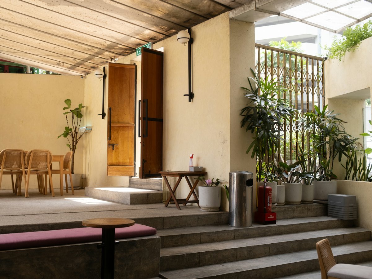 An open-air terrace with rattan chairs, timber doors and potted palms under a covered walkway.